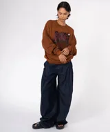 Buzo de algodón y poliéster color marrón con efecto tie-dye desgastado y estampado frontal con efecto glitter que dice "Get in GLAM". Presenta cuello redondo, puños y ruedo acanalados, y un bolsillo canguro.