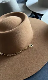 Sombrero negro de ala ancha y copa recta, confeccionado en lana merino uruguaya, con cadena dorada decorativa.