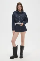 Campera corta de jean color negro con costuras a contratono en blanco, bolsillos frontales con solapa y cierre de botones metálicos.