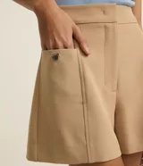 Short sastre de cintura alta color marrón, con bolsillos laterales y detalles de tachuelas metalizadas.