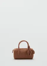 Bolso de mano tipo bowling de cuero gamuzado color marrón, con dos asas cortas y detalle de tiras con nudo y flecos colgantes en un lateral. Cierre superior con cremallera.
