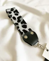 Llavero de tela con estampado animal print en tonos grises y negros, con pieza de cuero sintético negro y mosquetón metálico plateado.