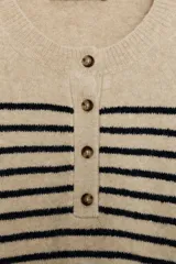 Jersey de punto de manga larga con cuello redondo y cierre frontal parcial con botones. Presenta un diseño a rayas horizontales en contraste sobre fondo beige.
