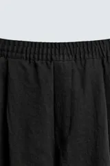 Pantalón negro de corte relajado con cintura elástica ajustable y pliegues en la parte delantera. Presenta bolsillos laterales y bolsillos traseros de parche.