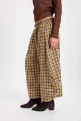 Pantalón de corte holgado con silueta tipo balloon, confeccionado en tela a cuadros. Presenta cintura elástica con cordón ajustable y cortes laterales circulares que aportan volumen a la prenda.
