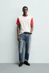 Remera de corte regular fit en color blanco con cuello redondo y mangas cortas en color rojo contrastante, y aplicación de parche bordado en el pecho.
