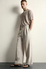 Pantalón relaxed fit de color blanco off-white, confeccionado en tejido con lino. Cuenta con pliegues frontales en la cintura, bolsillos delanteros y cierre frontal con cremallera y botón.