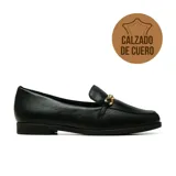 Zapato tipo mocasín de cuero negro con textura granulada, puntera redonda y detalle de herraje metálico dorado en el empeine. Cuenta con taco bajo plano.