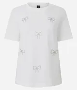 Remera de algodón de corte regular, con cuello redondo y mangas cortas. Presenta aplicaciones de lazos decorativos realizados con pedrería brillante en la parte frontal.