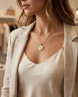 Collar de bronce dorado con cadena fina y dije redondo que presenta un fondo de nácar blanco y un trébol de cuatro hojas en el centro.