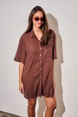 Vestido camisero corto de color marrón, con mangas cortas, cuello camisero, cierre frontal de botones y un bolsillo ojal en el pecho.