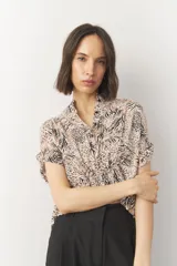 Blusa corta de manga corta con estampado en blanco y negro, cuello mao y cierre frontal con botones. Cuenta con detalle de elástico fruncido en la cintura que genera un efecto peplum.