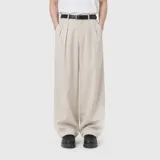 Pantalon sastrero de corte amplio y tiro alto, color beige, con pinzas frontales y cierre de cremallera. Confeccionado en denim de algodón con textura rústica.