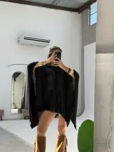 Poncho negro con capucha, confeccionado en tejido de punto abierto, con diseño amplio y caídas asimétricas.