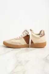 Zapatillas bajas color crema con puntera de gamuza beige, detalle de franja lateral en cuero marrón y contrafuerte en cuero metalizado color cobre.