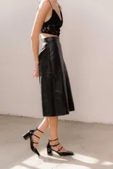 Pollera midi de eco cuero color beige, de corte recto y tiro alto, con costuras verticales decorativas y detalle de cinturón fino con flecos.