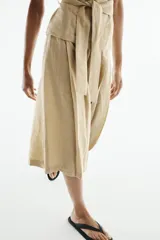 Bermuda de tiro alto color beige con trabillas en la cintura y detalle de pliegues en la parte delantera. Presenta un corte amplio y largo por debajo de las rodillas.
