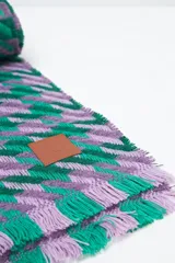 Bufanda rectangular con diseño a cuadros en tonos verde y lila, con flecos cortos en los extremos.