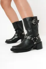 Bota biker de caña media color negro, con hebilla en la parte superior y detalle de aro y tachas en la parte inferior.