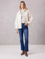 Campera bomber de eco cuero color beige, con cuello camisero, cierre frontal metálico y bolsillos delanteros con solapa y botón a presión. Presenta mangas largas con puños abotonados y ruedo trasero elastizado.