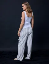 Pantalón cargo de lino a rayas verticales grises y blancas, marca Marissa Olivia. Pretina ancha elastizada con lazo de ajuste, bolsillos inclinados delanteros y bolsillos laterales con botón.