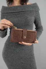 Billetera marrón con textura símil cocodrilo, cierre superior y broche con botón a presión. Tiene un bolsillo frontal, dos bolsillos con cierre en los extremos y dos bolsillos para tarjetas en el interior.