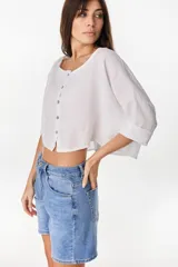 Camisa de lino azul marino, de corte crop y holgado, con cuello redondo, botonadura frontal y mangas amplias con vuelta.
