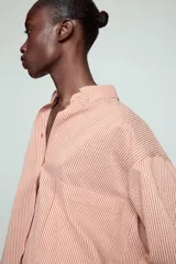 Camisa de cuello solapa y manga larga con estampado de rayas verticales. Presenta un bolsillo de plastrón en el delantero, cierre frontal con botones y detalle de botones en la espalda. Su diseño cuenta con un bajo asimétrico y aberturas laterales.