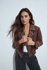Campera estilo biker de símil gamuza color marrón, con cierre frontal y detalles de tachas metálicas en solapas, mangas y ruedo.
