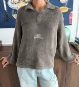 Sweater de textura suave y afelpada en color gris oscuro, con diseño de cuello redondo y mangas largas. Presenta un estampado gráfico en color blanco en la espalda con la inscripción 'odd studios'.