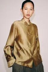 Camisa de estilo oriental confeccionada en mezcla de lyocell con acabado satinado. Presenta cuello redondo, manga larga con puños rectos, bolsillos de plastrón y cierre frontal mediante alamares.