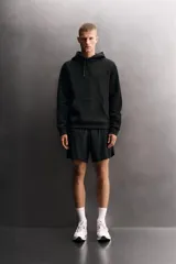 Sudadera de hombre Zara Athleticz de ajuste relajado (relaxed fit), color marrón, confeccionada en tejido técnico compacto con mezcla de algodón y elasticidad. Cuenta con cuello con capucha ajustable con cordones negros, manga larga, bolsillo frontal tipo canguro con un pequeño bolsillo termofijado con cierre, y acabados con rib en puños y cintura.