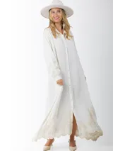 Maxi vestido camisero de lino blanco con bordados en tono beige en mangas y ruedo. Presenta cuello camisero, botones frontales y mangas largas.
