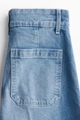 Jean de denim de algodón color azul con leve stretch, tiro alto, pierna amplia, bolsillos de parche traseros, pliegues delanteros y traseros, y doble botón en la cintura.