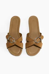 Sandalias planas color tostado, con tiras cruzadas y una hebilla metálica decorativa.
