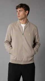 Campera bomber color beige, con cierre frontal metálico, bolsillos laterales ribeteados y puños, cuello y ruedo de rib elástico. Presenta un pequeño bordado al tono en el pecho.