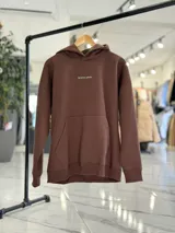 Canguro oversize marrón con capucha, bolsillo tipo canguro y diseño estampado en la espalda con el texto "Be Brave" y detalles tipográficos en color blanco.