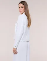 Camperita liviana de corte recto y acabado crepé color blanco, con cuello camisero clásico y cierre frontal de botones metálicos dorados. Presenta bolsillos en el pecho con solapa y mangas largas con puños abotonados.