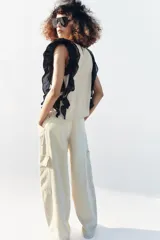 Blusa de cuello redondo y manga sisa, de color beige con rayas verticales. Presenta volantes negros en las sisas y una tira de encaje central con jaretas. Cuenta con cierre en la espalda con abertura y botón.