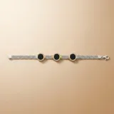 Pulsera de diseño articulado compuesta por eslabones de plata texturizada con detalles en oro y piedras circulares de ónix negro. El conjunto incluye además dos brazaletes rígidos complementarios en plata y oro.