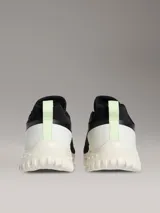 Zapatillas tipo runner Calvin Klein en color negro con suela de EVA blanca y detalles en verde claro en el talón. Presentan diseño tipo calcetín, parte superior de malla técnica y logo de la marca en la lengüeta y el lateral.