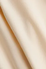 Top entallado de punto suave en color beige, con cuello tortuga, capa decorativa superpuesta y frunces laterales que generan un efecto drapeado.
