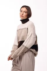Sweater de tejido de punto grueso con diseño de bloques de color en tonos beige, marrón y bordó. Presenta un corte relajado, mangas amplias y detalles de costuras visibles en contraste que separan las franjas de color.