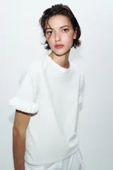 Camiseta de cuello redondo confeccionada en algodón, con mangas cortas decoradas con volantes en el mismo tejido y bajo recto.