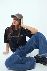 Remera de manga corta con silueta relajada y costuras a la vista en color blanco que contrastan sobre el tejido negro. Presenta un diseño moderno con terminaciones destacadas.