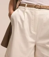 Short de sastrería color beige, de corte recto con pinzas delanteras y trabillas en la cintura. Incluye un cinturón de poliuretano a tono con hebilla metálica dorada.