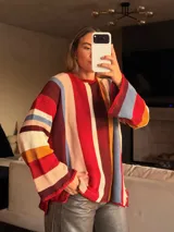 Sweater de punto tejido a mano con diseño de rayas verticales multicolores. Presenta silueta oversize, cuello a la base, mangas largas acampanadas y terminaciones en crochet en los bordes.