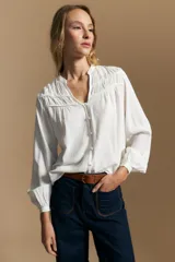 Camisa de manga larga color blanco, con cuello mao y escote en V. Presenta frunces en el canesú, cierre frontal con botones y mangas amplias con puños abotonados.