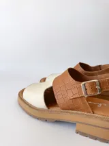 Sandalia de cuero color camel y crudo, con tira ancha sobre los dedos, tira al tobillo con hebilla y suela track.