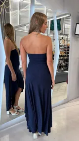 Vestido largo azul marino con acabado brillante, diseño strapless y corte asimétrico con volados en la falda.